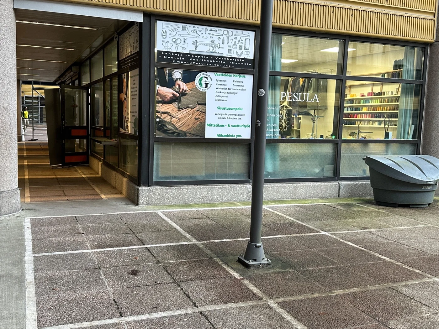 Green Ompelimon mainosikkuna, PESULA-teksti ja ovi vasemmalla katetun kulkuväylän puolella
